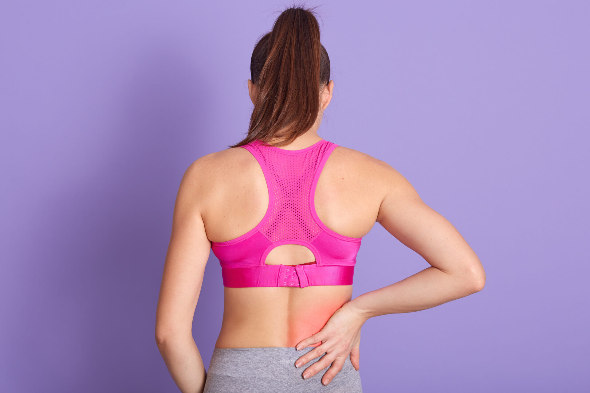 Rear view of a woman in activewear experiencing lower back pain
