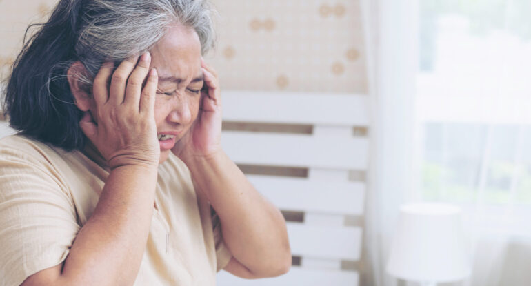 Senior woman experiencing symptoms of a migraine headache, holding her temples in pain