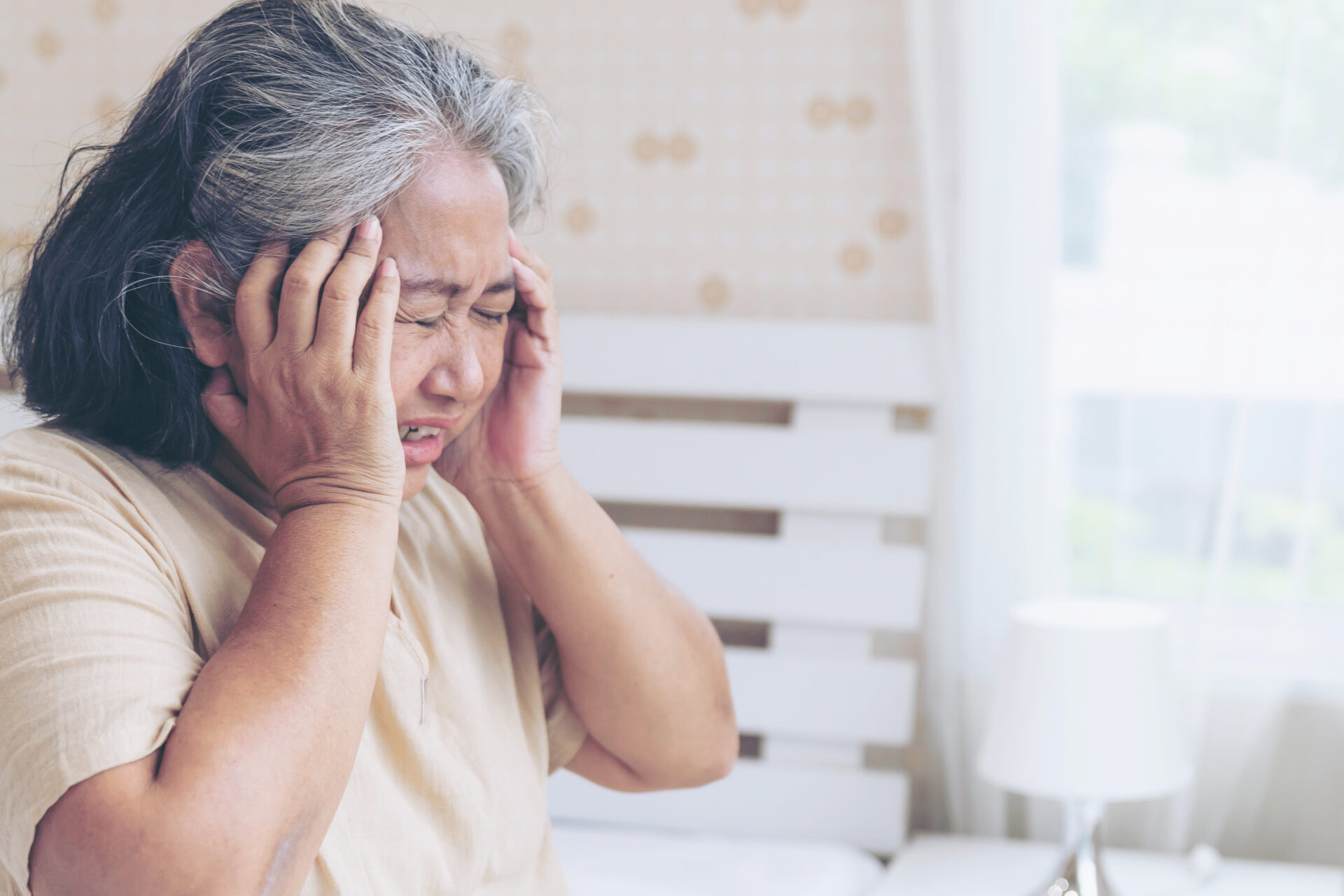 Senior woman experiencing symptoms of a migraine headache, holding her temples in pain